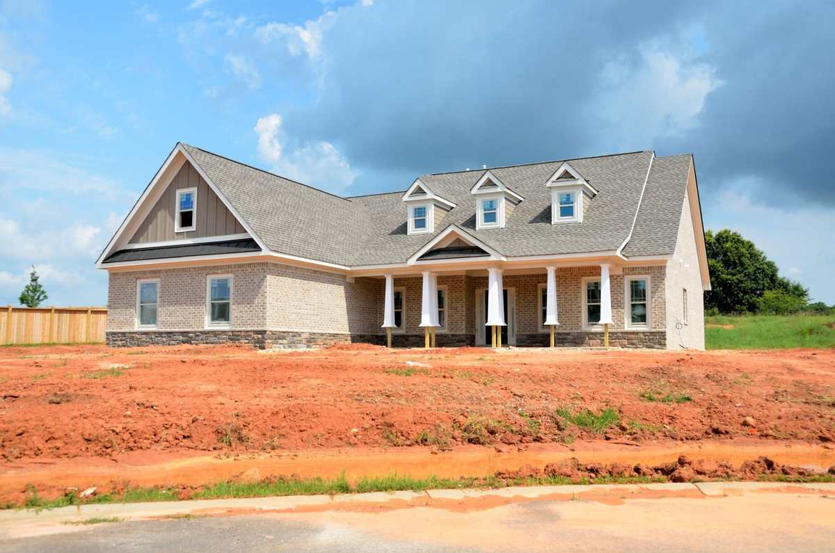 Maison en construction avec toit gris et colonnes blanches sur un terrain enclavé