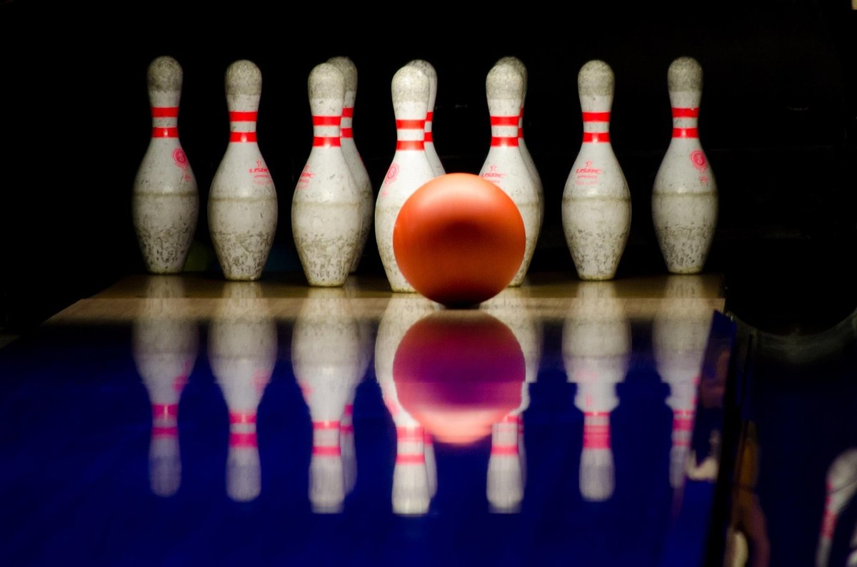 Une balle orange prête à frapper dix broches alignées sur une piste sombre Une balle orange prête à frapper dix broches alignées sur une piste sombre