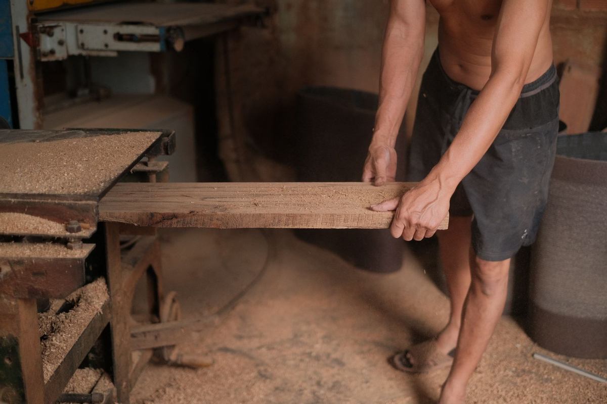 Homme ponçant une planche dans un atelier de menuiserie Homme ponçant une planche dans un atelier de menuiserie