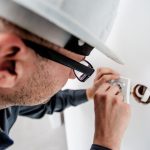 Homme en casque et lunettes manipulant un objet dans un trou de mur