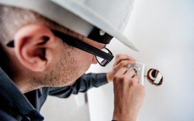 Homme en casque et lunettes manipulant un objet dans un trou de mur