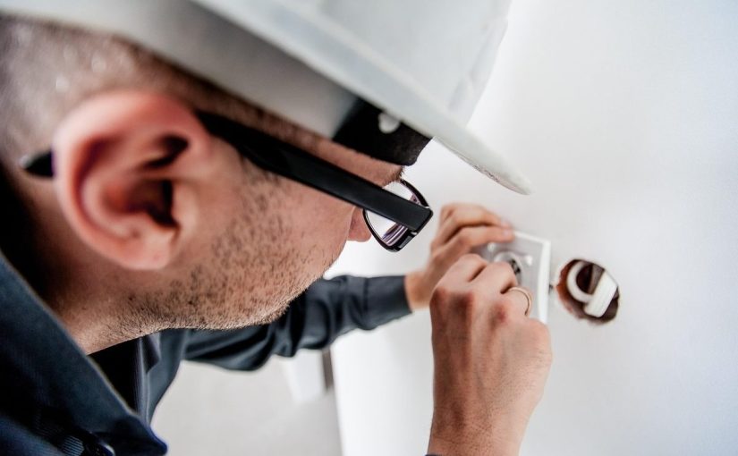Homme en casque et lunettes manipulant un objet dans un trou de mur