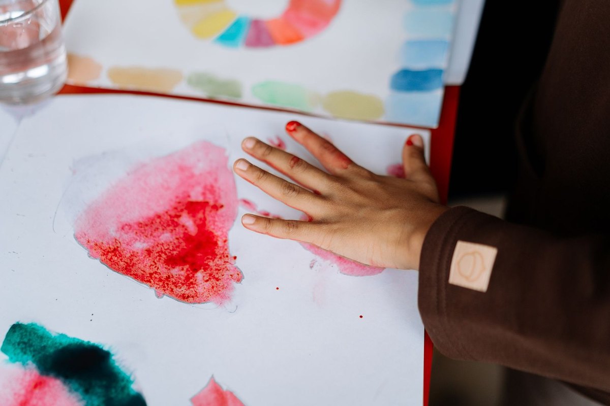 main colorée sur papier avec empreintes, palette et verre d'eau à proximité main colorée sur papier avec empreintes, palette et verre d'eau à proximité