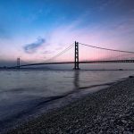 Un pont suspendu au crépuscule au-dessus d'une plage de galets avec quelques personnes