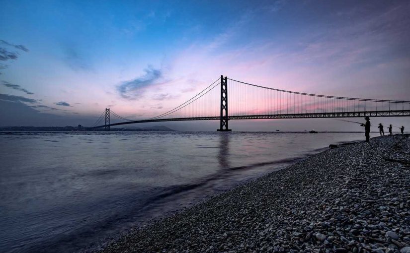 Un pont suspendu au crépuscule au-dessus d'une plage de galets avec quelques personnes