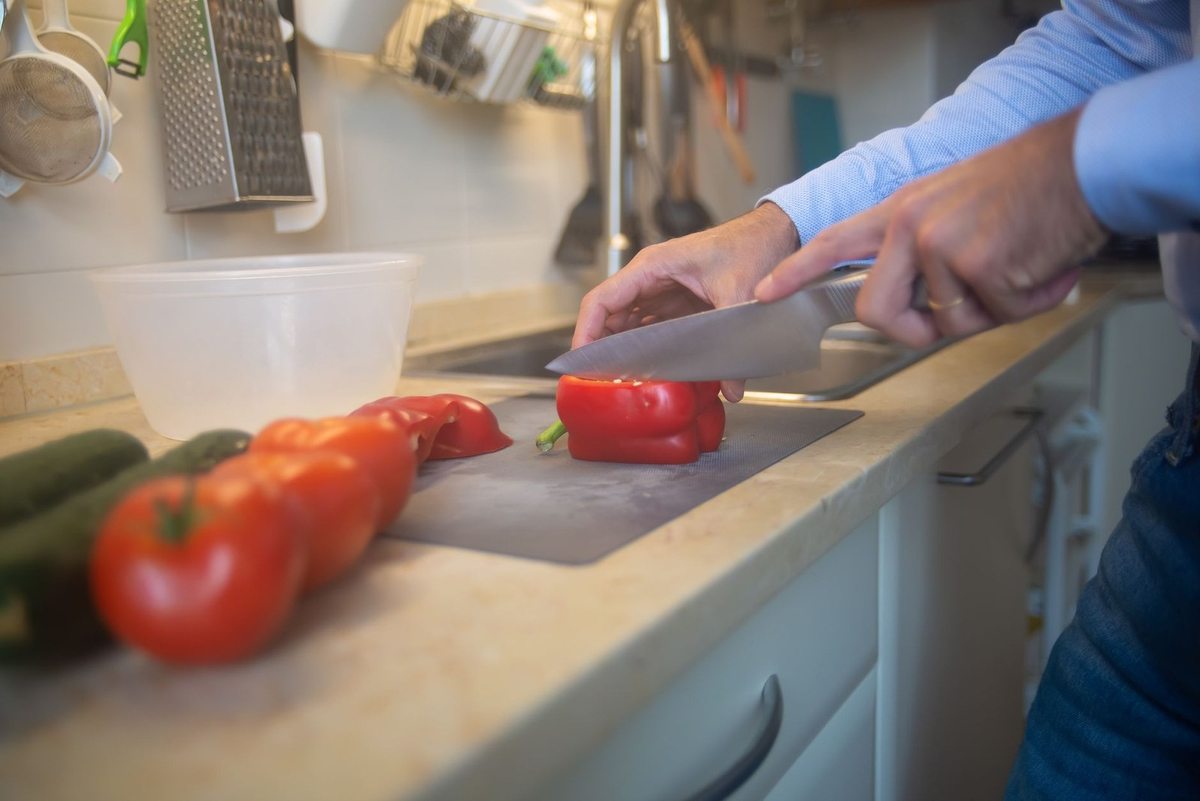 Personnage tranchant un poivron rouge sur une planche à découper, tomates et concombres à proximité Personnage tranchant un poivron rouge sur une planche à découper, tomates et concombres à proximité