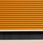 fenêtre avec volet roulant orange partiellement abaissé cadre blanc vitre sombre